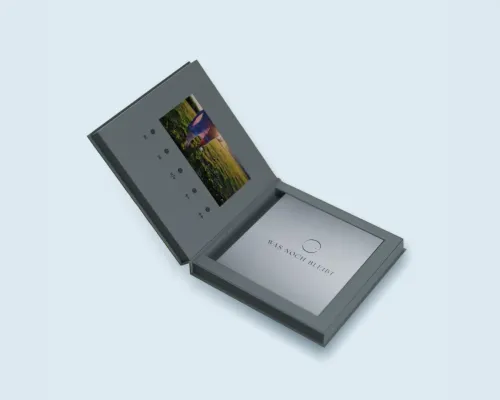 Geöffnete graublaue Videobox mit integriertem Display und dem passgenau eingelegten Erinnerungsbuch „Was noch bleibt“ aus der Vogelperspektive.